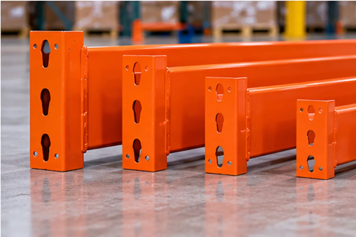 Four orange pallet rack beams of different lengths and face heights lined up on a warehouse floor